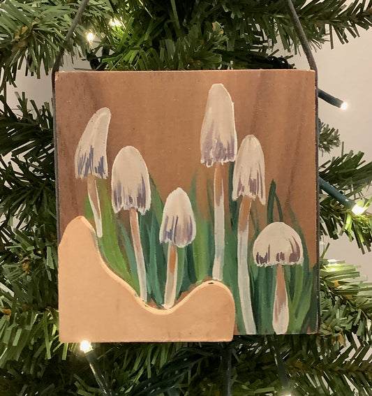 Wooden ornament with painted mushrooms hanging on a Christmas tree.